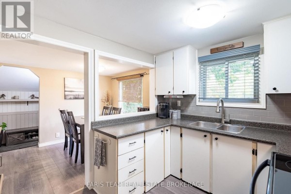 Kitchen showing white cabinets and dark countertops, with a pass-through window to a dining area and living room. - 244/250 Dignard Avenue, Tay