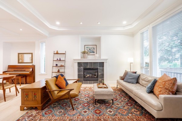 Living room with a sectional sofa, fireplace, red rug, and open-plan kitchen in background. - 2440 124b Street, Surrey