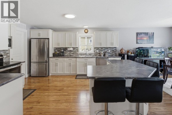Kitchen with white cabinets, stainless steel appliances, island with bar stools, and backsplash. - 2440 Old Okanagan Highway Unit# 523, West Kelowna