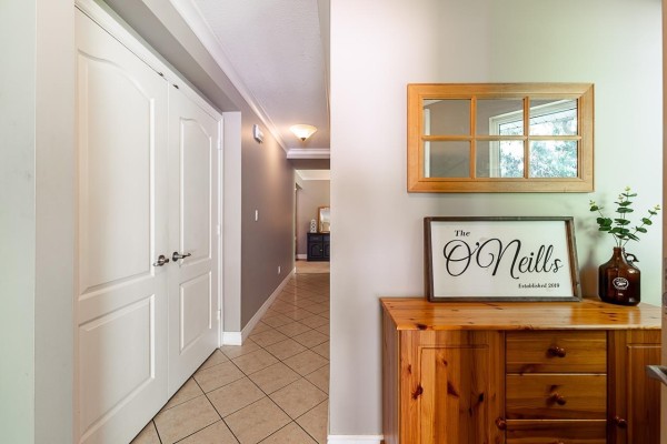 Hallway inside a home with beige tile floors, white double doors, and wooden furniture with decor. - 24400 56 Avenue, Langley
