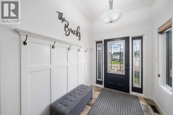 Interior foyer with white paneled walls, coat hooks, a grey bench, and a black front door. - 2448 7 Avenue Ne, Medicine Hat