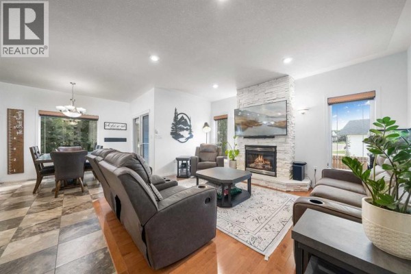 Living room with grey recliners, a stone fireplace with a television, and a dining area. - 2448 7 Avenue Ne, Medicine Hat