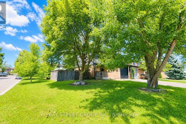 Green lawn and trees in front of a townhouse entrance under a blue sky. - 245 Browning Trail, Barrie