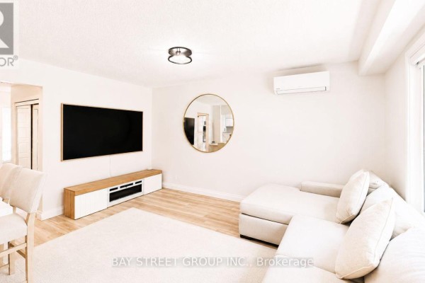 Bright living room with a sectional sofa, large TV, and light wood flooring. - 245 Browning Trail, Barrie