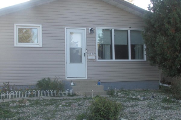 Front facade of the beige bungalow showing the door, windows, and entrance steps. - 245 Edward Street, Regina