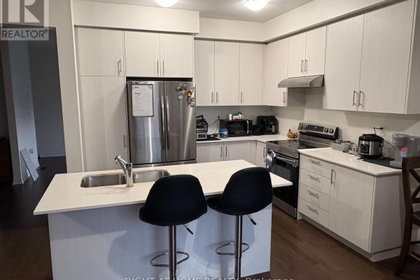 A kitchen with light wood cabinets, a stainless steel refrigerator, and a white island. - 245 Madelaine Drive, Barrie