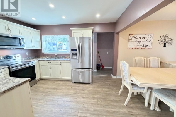Kitchen and dining area with white cabinets, stainless steel appliances, and a dining table. - 245 Maple Street S, Timmins