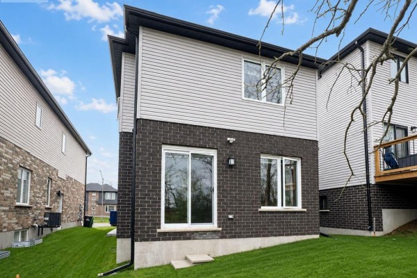Rear exterior of a modern house with grey siding, dark brick, and a sliding glass door. - 245 Wesley Boulevard, Cambridge