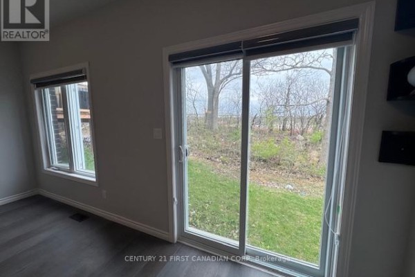 Living room with a sliding glass door and a window offering views of a wooded backyard area. - 245 Wesley Boulevard, Cambridge