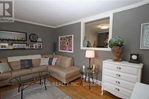 Living room with a large sectional sofa, glass coffee table, and a white dresser with decorative items. - 245 Windsor Street, Oshawa