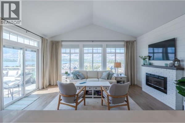 Sunlit living room with a view, showcasing a fireplace and built-in cabinetry - 2450 Radio Tower Road Unit# 174, Oliver