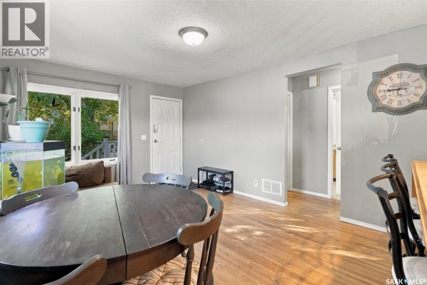 Living and dining area with hardwood floors, grey walls, and a large window. - 2451 Francis Street, Regina