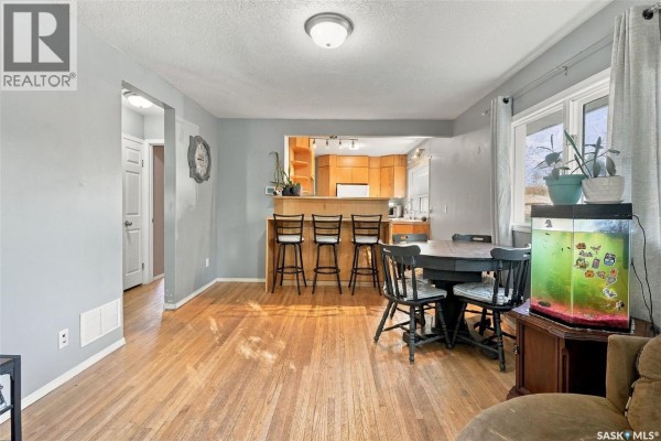 View of living area, dining table, kitchen pass-through with bar stools, and hallway. - 2451 Francis Street, Regina