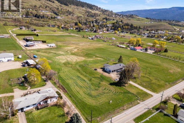 Aerial view of a large, grassy parcel of land with mowed patterns, surrounded by houses and mountains. - 2455 East Vernon Road, Vernon