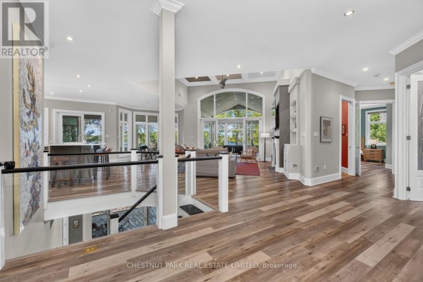 Interior view of a spacious, open-concept living area with hardwood floors, light grey walls, and large windows overlooking a lake. - 2458 Wilkinson Road, Dysart Et Al