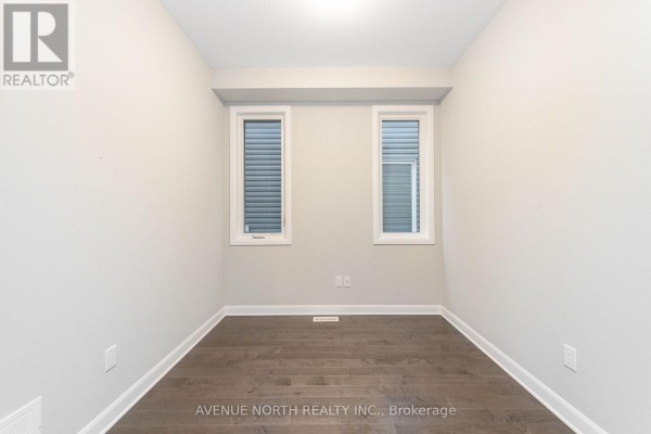 Empty room with grey walls, dark hardwood floor, and two narrow windows with blinds. - 246 Aquarium Avenue, Ottawa