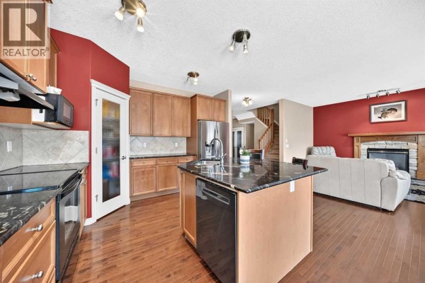 View of the kitchen and living area with a fireplace, couch, and stairs leading upstairs. - 246 Crystal Green Point, Okotoks