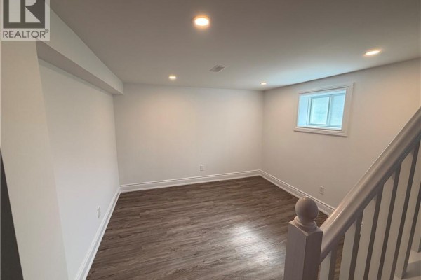 Another view of the finished basement with white walls, wood-look flooring, and a small window. - 246 East 27th Street, Hamilton