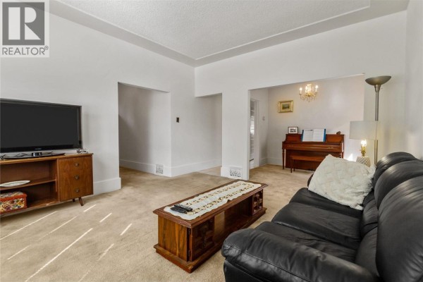 Living room showing a television, entryway, and a piano in an adjacent room. - 2461 Dundas Street, Vancouver