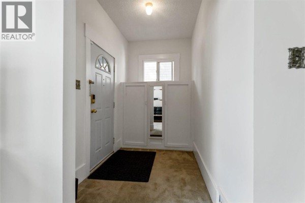 Entrance hallway with a white door, shoe cabinet, and beige carpet. - 2461 Dundas Street, Vancouver