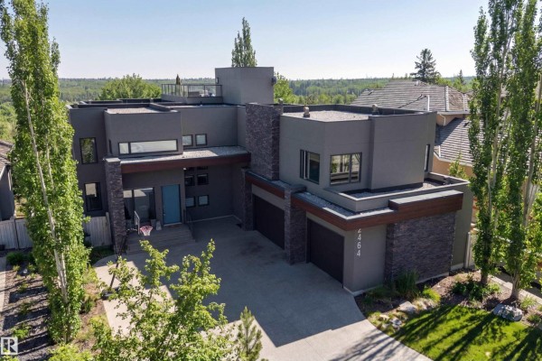 Aerial view of a large modern house with a grey stucco exterior, stone accents, and three garage doors. - 2464 Cameron Ravine Dr Nw, Edmonton
