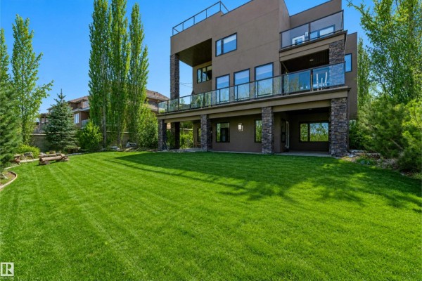 Rear view of the house with multiple levels of balconies, glass railings, and a spacious green backyard. - 2464 Cameron Ravine Dr Nw, Edmonton