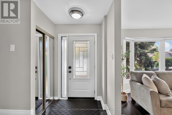 Interior foyer with a glass-panelled door, mirrored closet, and a grey couch. - 2467 Grindstone Court, Mississauga