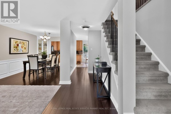 Hallway view showing the dark wood floor, grey carpeted stairs, and a dining room. - 2467 Grindstone Court, Mississauga