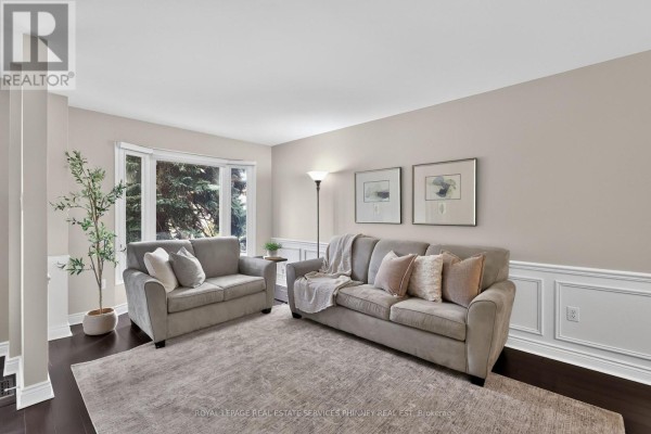 Living room with two grey sofas, a large bay window, white wainscoting, and artwork. - 2467 Grindstone Court, Mississauga