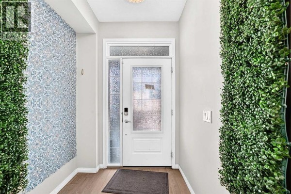 Interior view of the front entryway with patterned wallpaper and faux greenery flanking the white door. - 247 Cityscape Way Ne, Calgary