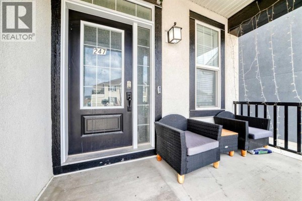 Covered front porch with black wicker chairs, a small table, and a black front door. - 247 Cityscape Way Ne, Calgary