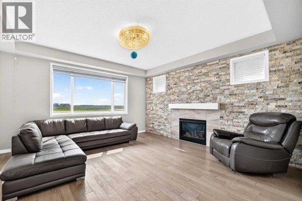 Living room featuring a large sectional sofa, leather recliner, gas fireplace, and stone accent wall. - 247 Cityscape Way Ne, Calgary