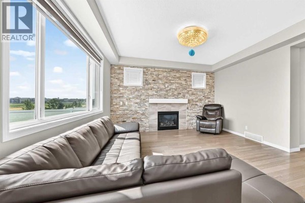 Living room with a sectional sofa, leather armchair, fireplace, and large windows with an outdoor view. - 247 Cityscape Way Ne, Calgary
