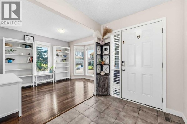 Entranceway with dark hardwood floors, white doors, built-in bookshelves, and large bay windows. - 247 Cranberry Place Se, Calgary