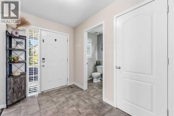 Entranceway with tiled floors, a white door, a shelving unit, and a doorway to a half bathroom. - 247 Cranberry Place Se, Calgary