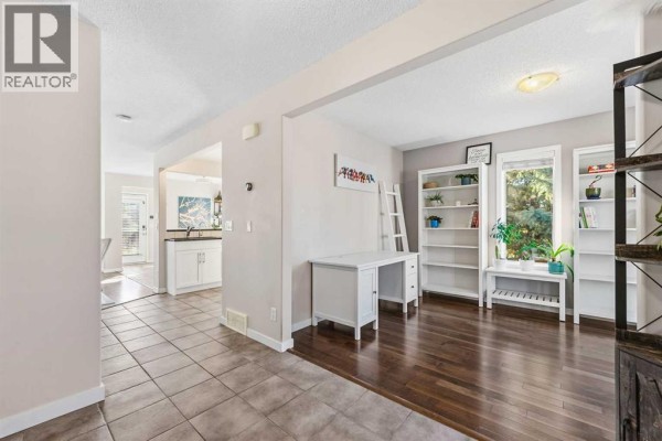 Living area with dark hardwood floors, white furniture, built-in bookshelves, and large windows. - 247 Cranberry Place Se, Calgary