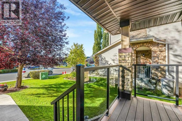 Covered front porch with dark railing, glass panels, and stone pillars. - 247 Crystal Shores Drive, Okotoks