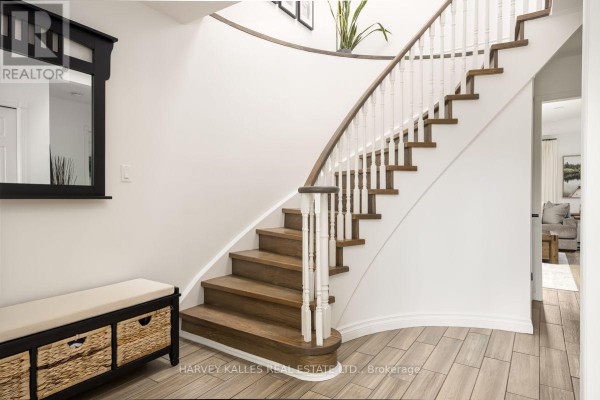 Curved wooden staircase with white spindles and a dark wood handrail, in a white foyer. - 247 Overbank Drive, Oshawa