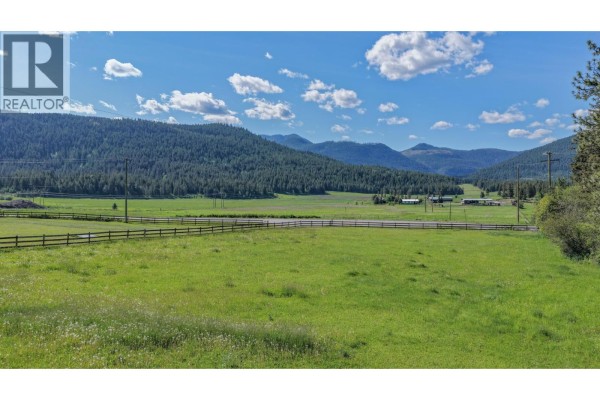 View of rolling green fields, distant mountains, and a blue sky with clouds. - 2471 6 Highway, Lumby