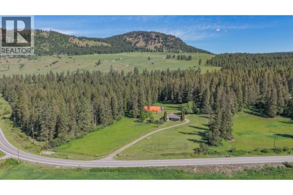 Aerial view of a rural property with a house, outbuildings, and surrounding forest. - 2471 6 Highway, Lumby