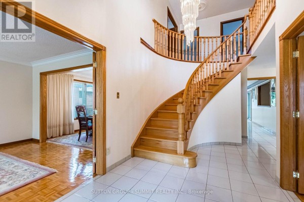 Interior foyer with a curved wooden staircase, white tile floor, and crystal chandelier. - 2477 Cliff Road, Mississauga