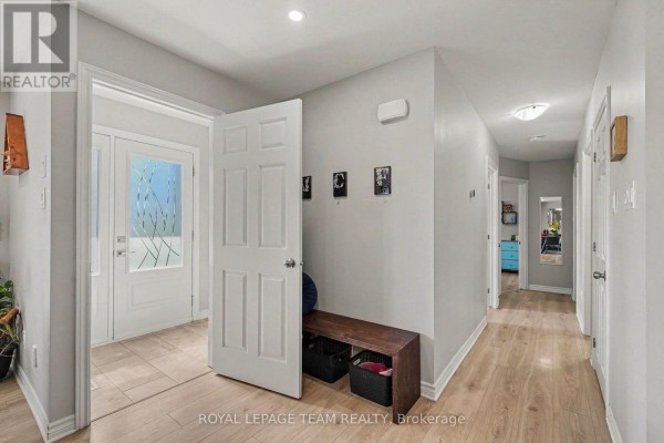Interior hallway with light wood floors, white doors, and a bench with storage baskets. - 2477 Merivale Road, Ottawa