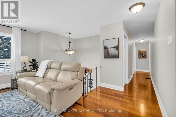 Living room area with beige leather sofa, hardwood floors, and a hallway with two framed pictures. - 2477 Old Fort Road, Tay
