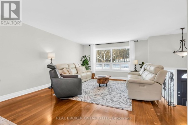 Living room with leather sofas, a grey armchair, patterned rug, and a large window with a view of trees. - 2477 Old Fort Road, Tay