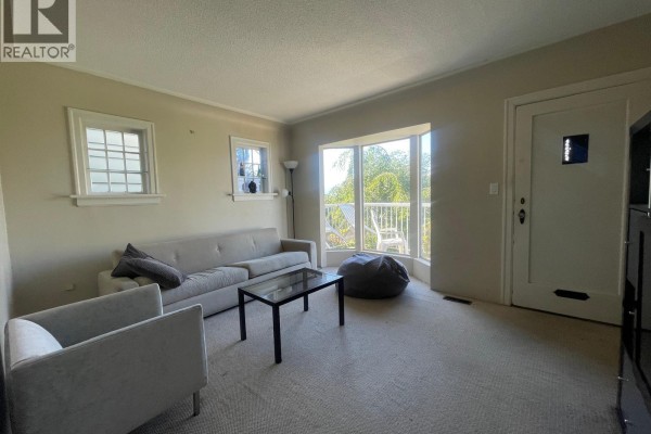 Living room with a beige sofa, two armchairs, a glass coffee table, and large bay windows. - 2478 E 28th Avenue, Vancouver
