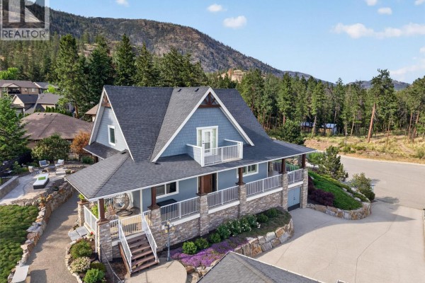 Front view of the house showcasing the stone foundation, covered porch with white railings, and gray siding. - 2478 Stone Grove Crescent, West Kelowna