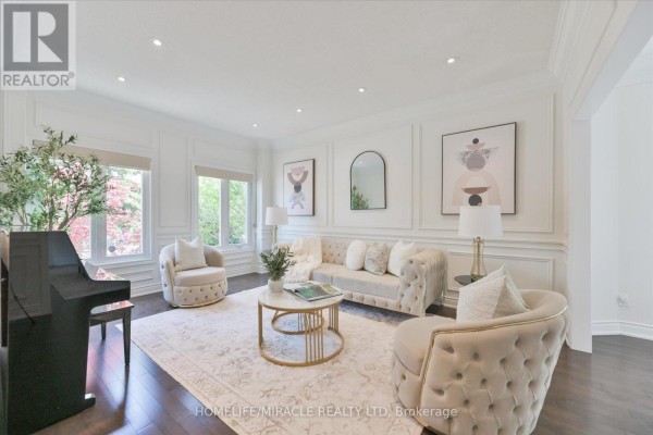 Living room with plush beige furniture, a black piano, decorative wall molding, and large windows. - 2479 Rathlin Court, Mississauga