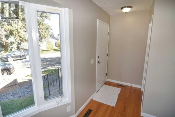Interior view of a home's entryway with light beige walls and hardwood flooring. - 248 Bracewood Road Sw, Calgary