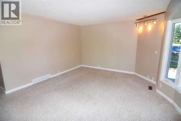 Empty living room with beige carpeting, beige walls, and a large bay window. - 248 Bracewood Road Sw, Calgary