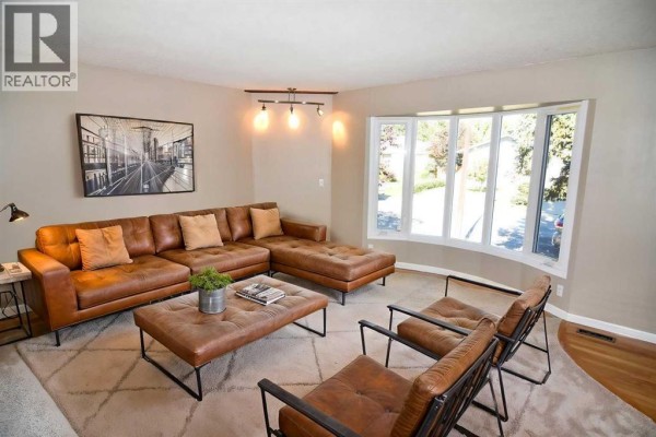 Living room with a large sectional sofa, coffee table, chairs, and bay window. - 248 Bracewood Road Sw, Calgary
